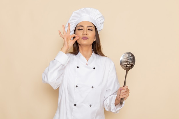 Foto gratuita vista frontal de la joven cocinera en traje de cocinero blanco sosteniendo una cuchara de plata grande en la pared blanca