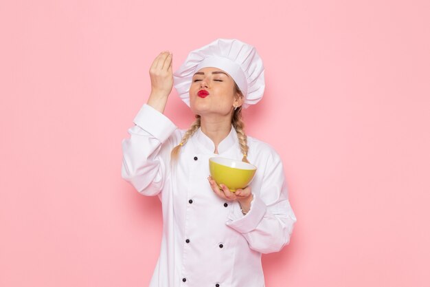 Vista frontal joven cocinera en traje de cocinero blanco sosteniendo placa verde en el cocinero espacial rosa