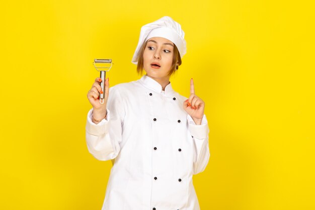 Una vista frontal joven cocinera en traje de cocinero blanco y tapa blanca con limpiador vegetal posando en el amarillo
