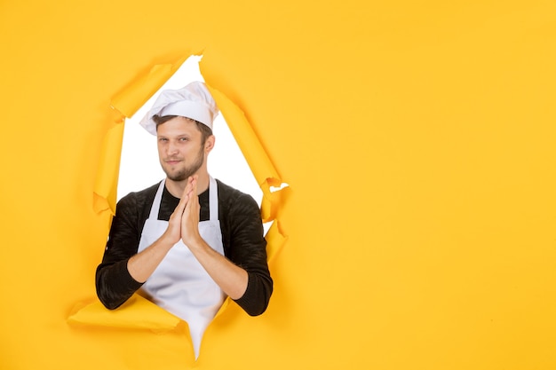 Vista frontal joven cocinero en capa blanca y gorra sobre fondo amarillo comida hombre blanco cocina foto color trabajo de cocina