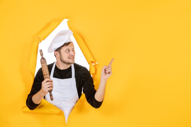 Vista frontal joven cocinero en capa blanca sosteniendo rodillo sobre fondo amarillo foto comida hombre blanco cocina trabajo color