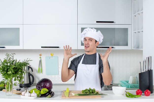 Vista frontal joven cocinero insatisfecho en uniforme en la cocina