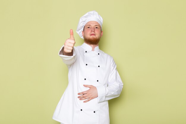 Una vista frontal joven cocinero masculino en traje de cocinero blanco gorra blanca que muestra un signo impresionante