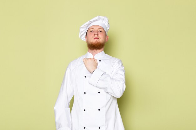 Una vista frontal joven cocinero masculino en traje de cocinero blanco tapa de cabeza blanca arreglando su paño
