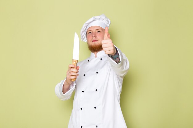 Una vista frontal joven cocinero de sexo masculino en traje de cocinero blanco cabeza blanca tapa con cuchillo