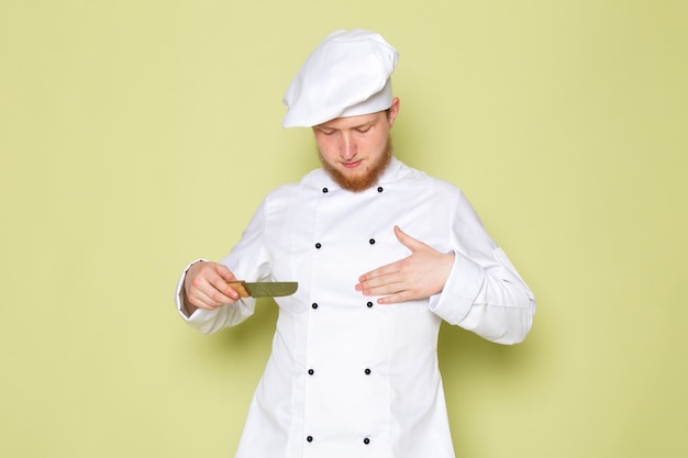 Una vista frontal joven cocinero de sexo masculino en traje de cocinero blanco cabeza blanca tapa con cuchillo