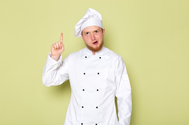Una vista frontal joven cocinero en traje de cocinero blanco gorra blanca con el dedo levantado