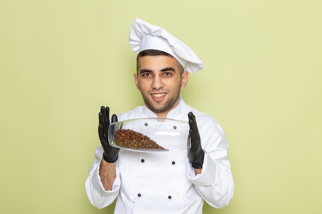 Vista frontal joven cocinero en traje de cocinero blanco con guantes oscuros y sosteniendo café en verde