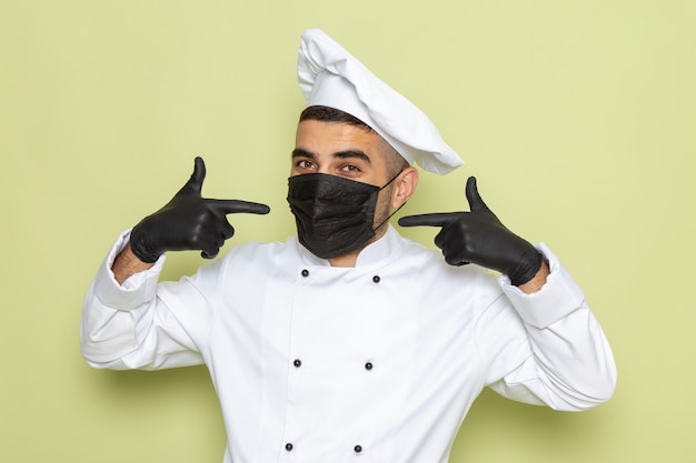 Foto gratuita vista frontal joven cocinero en traje de cocinero blanco con máscara y guantes en verde