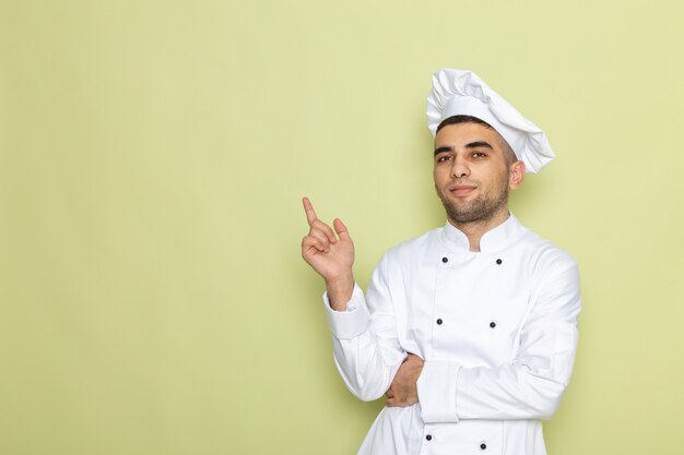 Vista frontal joven cocinero en traje de cocinero blanco de pie con expresión de pensamiento en verde