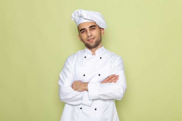 Vista frontal joven cocinero en traje de cocinero blanco posando con los brazos cruzados en verde