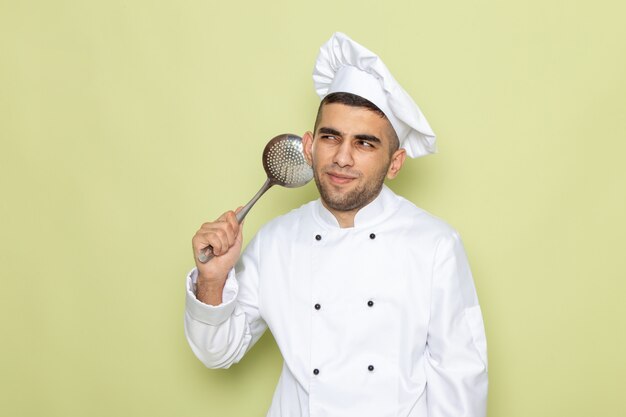 Vista frontal joven cocinero en traje de cocinero blanco posando con expresión de pensamiento en verde