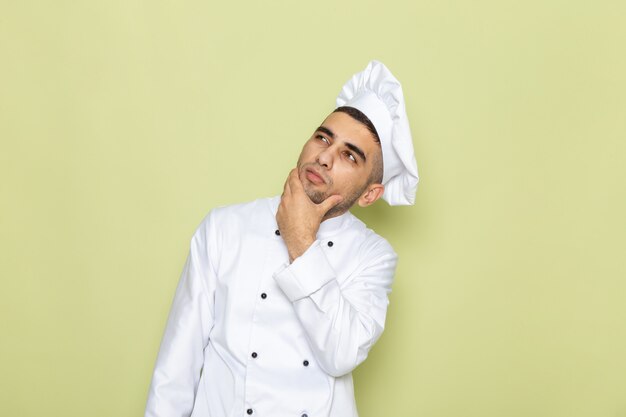 Vista frontal joven cocinero en traje de cocinero blanco posando y pensando en verde