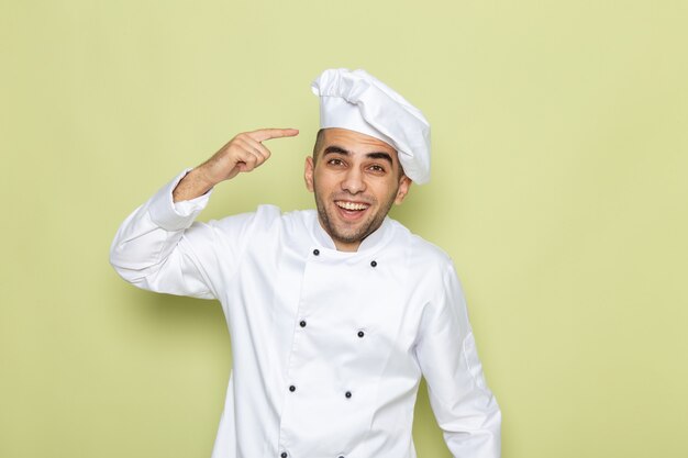 Vista frontal joven cocinero en traje de cocinero blanco posando con sonrisa en verde