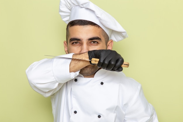 Foto gratuita vista frontal joven cocinero en traje de cocinero blanco sosteniendo un cuchillo con guantes en verde