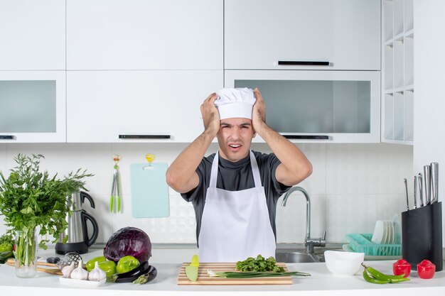 Vista frontal joven cocinero en uniforme sosteniendo su cabeza