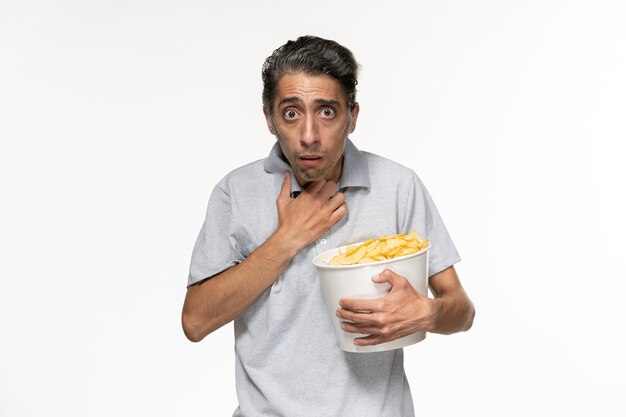 Vista frontal joven comiendo papas fritas viendo la película sobre una superficie blanca clara