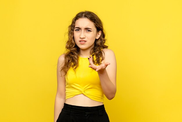 Vista frontal de la joven confundida en la pared amarilla