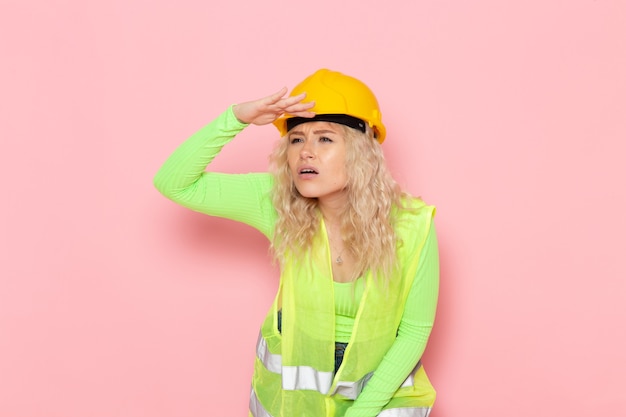 Vista frontal joven constructora en traje de construcción verde casco amarillo mirando a la distancia en el trabajo de construcción de arquitectura de trabajo espacial rosa