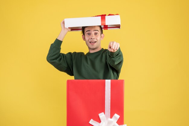 Vista frontal joven cubriendo su cabeza de pie detrás de una gran caja de regalo en amarillo