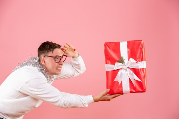 Vista frontal del joven dando regalo de Navidad a alguien en la pared rosa