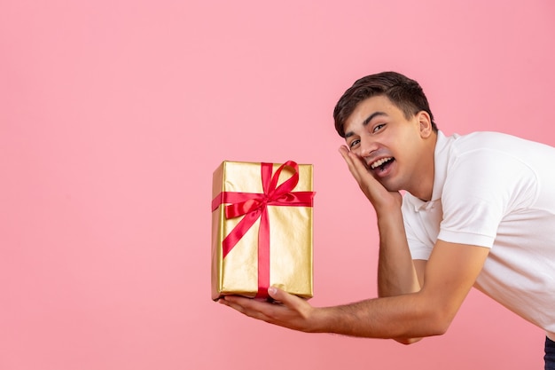 Vista frontal del joven dando regalo de Navidad a alguien en la pared rosa