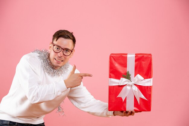 Vista frontal del joven dando regalo de Navidad a alguien en la pared rosa