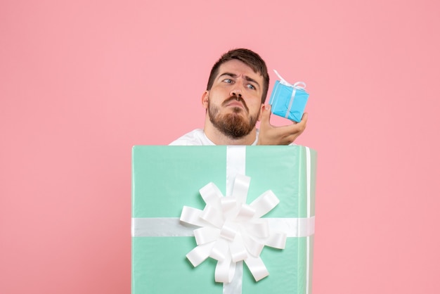 Vista frontal del joven dentro de la caja actual con pequeño regalo en la pared rosa