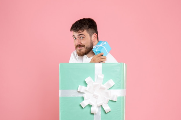 Vista frontal del joven dentro de la caja actual con pequeño regalo en la pared rosa