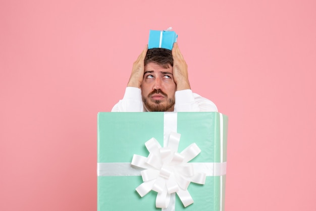 Vista frontal del joven dentro de la caja actual con pequeño regalo en la pared rosa