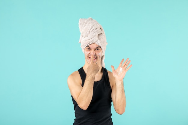 Vista frontal del joven después de la ducha con crema en la cara en la pared azul