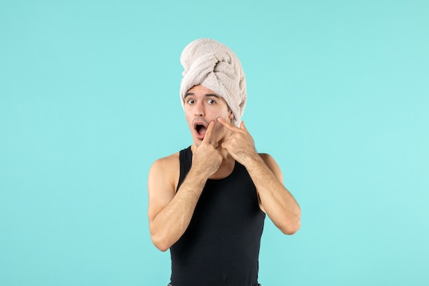 Vista frontal del joven después de la ducha con grano en la cara en la pared azul