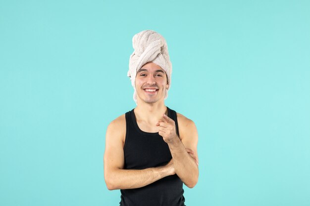 Vista frontal del joven después de la ducha sonriendo en la pared azul