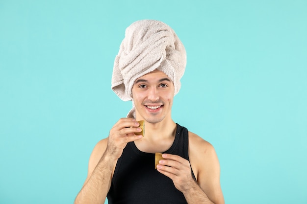 Vista frontal del joven después de la ducha sosteniendo rodajas de kiwi en la pared azul