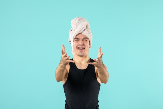 Vista frontal del joven después de la ducha con una toalla en la cabeza llorando en la pared azul
