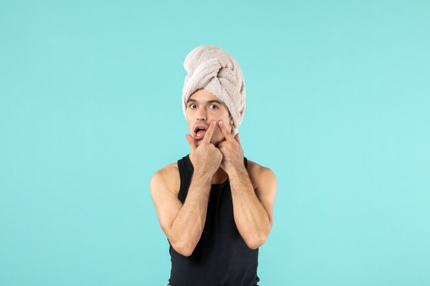 Vista frontal del joven después de la ducha con una toalla en la cabeza en la pared azul