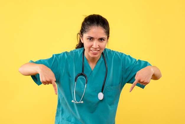 Vista frontal de la joven doctora apuntando a la pared. en la pared amarilla