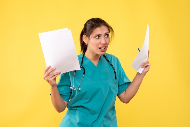 Vista frontal joven doctora en camisa médica con análisis de papel sobre fondo amarillo