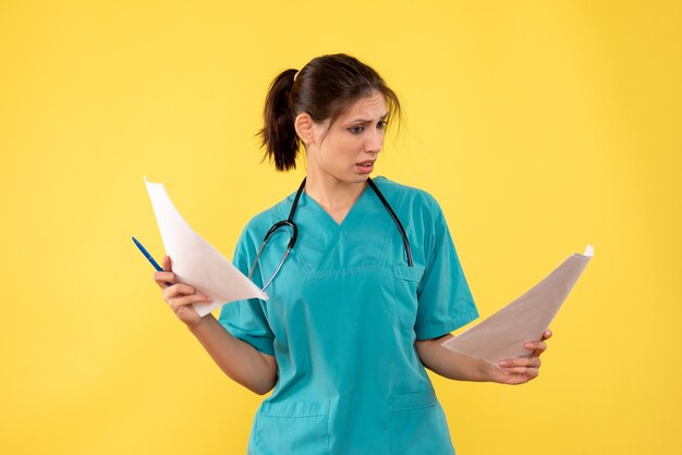 Vista frontal joven doctora en camisa médica con análisis de papel sobre fondo amarillo