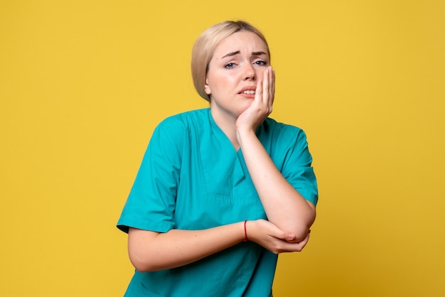 Vista frontal de la joven doctora en camisa médica con brazo herido en pared amarilla