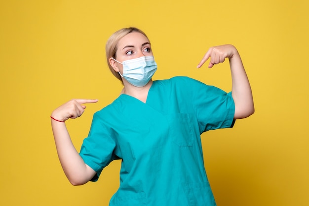 Vista frontal de la joven doctora en camisa médica y máscara en la pared amarilla