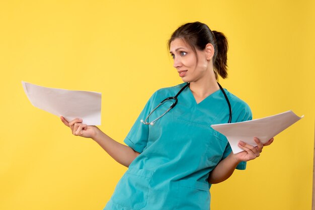 Vista frontal joven doctora en camisa médica con papeles sobre fondo amarillo