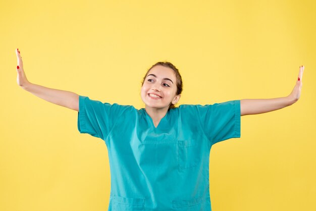 Vista frontal de la joven doctora en camisa médica en la pared amarilla