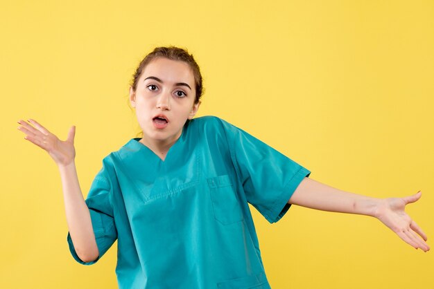 Vista frontal de la joven doctora en camisa médica en la pared amarilla