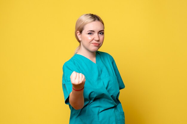Vista frontal de la joven doctora en camisa médica en la pared amarilla