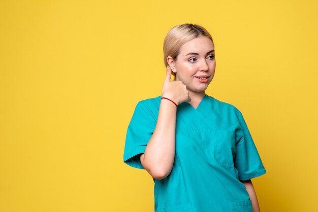 Vista frontal de la joven doctora en camisa médica en la pared amarilla