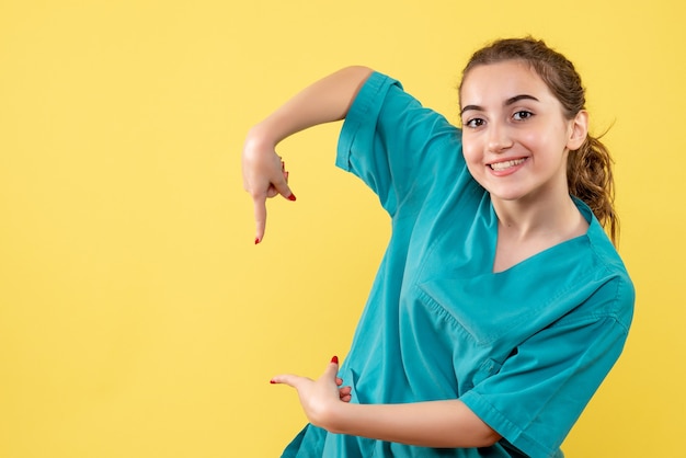 Vista frontal de la joven doctora en camiseta médica sonriendo en la pared amarilla