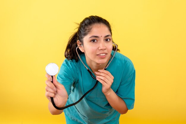 Vista frontal de la joven doctora con estetoscopio en pared amarilla
