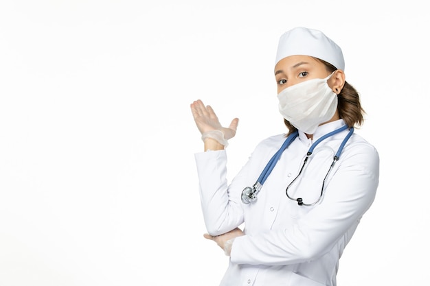 Vista frontal joven doctora con máscara estéril y guantes debido al coronavirus en el escritorio blanco