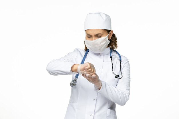 Vista frontal joven doctora con máscara estéril y guantes debido al coronavirus en la superficie blanca